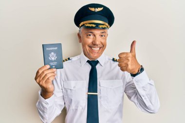 Yakışıklı orta yaşlı olgun pilot elinde pasaportuyla mutlu ve olumlu gülümsüyor, başparmağıyla mükemmel ve onay işareti yapıyor. 