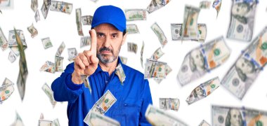 Orta yaşlı, tamirci üniforması giyen yakışıklı bir adam parmağını kaldırmış ve kızgın bir ifade takınıyor.