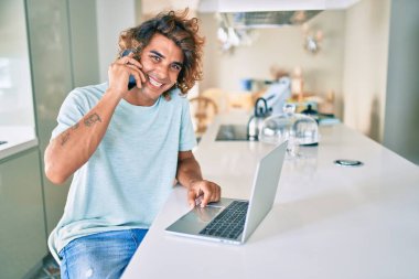 Genç İspanyol adam evde akıllı telefon ve dizüstü bilgisayar kullanıyor..