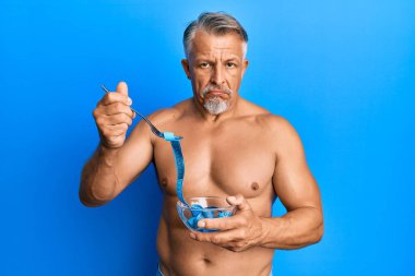 Orta yaşlı, gri saçlı, gömleksiz bir adam kilo vermek için diyet yapıyor. Depresyonda ve üzüntüden ağlıyor, ağlıyor ve korkuyor. hüzünlü ifade. 