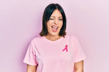 Tişörtüne pembe kanser kurdelesi takmış genç İspanyol kadın kameraya seksi bir ifadeyle bakıyor, neşeli ve mutlu bir yüzle.. 