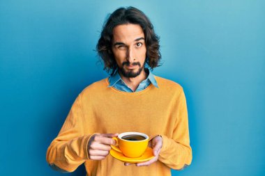 Latin asıllı genç bir adam bir fincan kahve içiyor şüpheci ve gergin, sorun yüzünden surat asıyor. negatif kişi. 