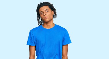 Gündelik kıyafetler giyen genç Afro-Amerikan adam yüzünde ciddi bir ifadeyle rahatlamış. Basit ve doğal bir şekilde kameraya bakıyorsun.. 