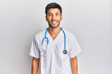 Doktor üniforması giyen genç yakışıklı bir adam ve yüzünde mutlu ve havalı bir gülümsemeyle steteskop. şanslı kişi. 
