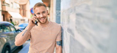 Genç İrlandalı gülümseyen mutlu bir adam şehrin caddesinde akıllı telefonda konuşuyor..