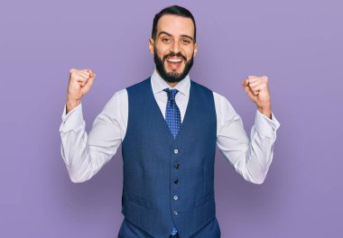 Sakallı, iş yeleği giyen genç adam kollarını kaldırıp, gözleri açık bir şekilde başarıyı kutluyor ve hayrete düşüyor. Kazanan konsept. 