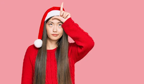 若いです中国の女性身に着けていますクリスマス帽子作る楽しみますの人々とともに指オン額ド負け犬ジェスチャーモックと侮辱 — ストック写真