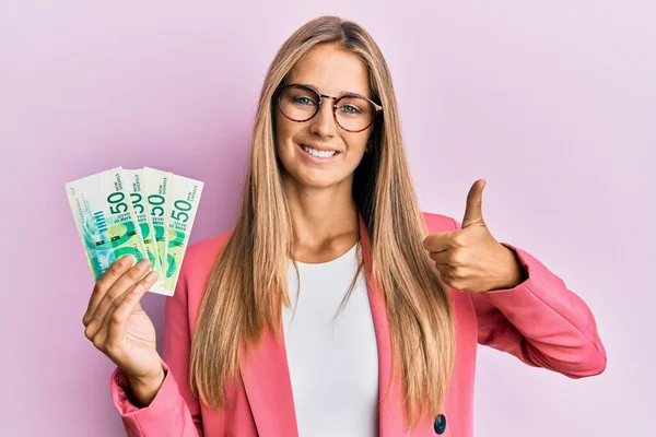 年轻的金发女郎 身穿商务风格的衣服 手里拿着伊斯莱尔 谢克尔 面带微笑 面带微笑 泰然自若 泰然自若 泰然自若 — 图库照片