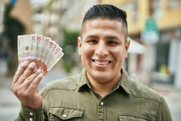 Young latin man smiling happy holding colombian pesos at the city.