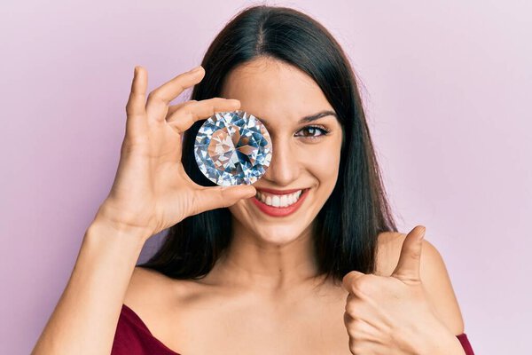 Молодая латиноамериканка с бриллиантовым камнем на глазу улыбается счастливой и позитивной, большой палец вверх делает отлично и знак одобрения 