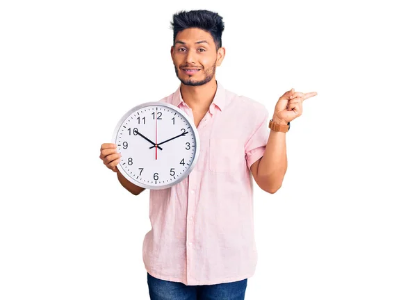 Bonito Jovem Latino Americano Segurando Grande Relógio Sorrindo Feliz Apontando — Fotografia de Stock