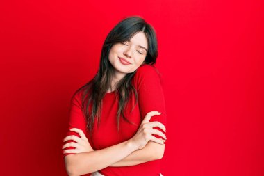 Genç, güzel, beyaz, sıradan kırmızı tişörtler giyen mutlu, pozitif ve kendinden emin bir şekilde kendine sarılan bir kız. Sevgi ve özgüven. 