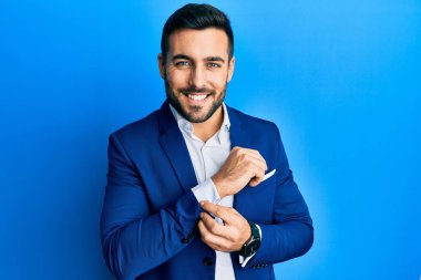 Genç İspanyol iş adamı iş ceketi giyiyor gömlek düğmesi takıyor mutlu ve havalı bir gülümsemeyle gülümsüyor. diş gösterme. 