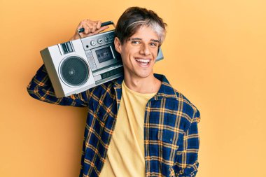 Kasetçalar tutan genç İspanyol adam, pozitif ve mutlu görünerek müzik dinliyor ve kendine güvenen bir gülümsemeyle dişlerini gösteriyor. 