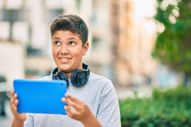 Sevimli Latin çocuk mutlu bir şekilde gülüyor. Parkta kulaklık ve dokunmatik ped kullanıyor..