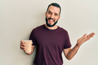 Sakallı genç adam bir fincan kahve içerek başarıyı kutluyor mutlu bir gülümsemeyle ve kazanan yüz ifadesiyle elini kaldırarak. 