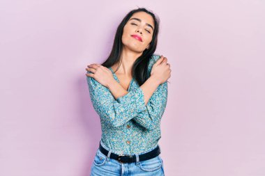 Gündelik kıyafetler giyen genç İspanyol kız kendine sarılıyor mutlu ve pozitif, kendinden emin gülümsüyor. Sevgi ve özgüven. 