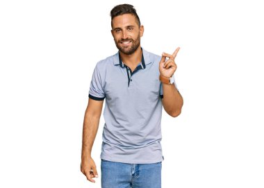 Sakallı, sıradan kıyafetler giyen, yüzünde kocaman bir gülümseme olan, eli kameraya bakan yakışıklı bir adam.. 