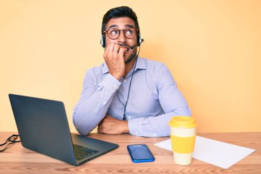 Çağrı merkezinde çalışan operatör kulaklığı takan İspanyol genç adam elleri ağızda çivi yerken gergin ve stresli görünüyor. anksiyete. 
