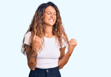 Kolları havada ve gözleri kapalı zaferi kutlayan gülümseyen, sıradan beyaz tişörtlü İspanyol bir kadın. Kazanan konsept. 