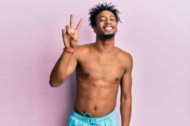 Sakallı, mayolu, gülümseyen, kameraya göz kırpan, zafer işareti yapan Afro-Amerikan genç adam. İki numara.. 