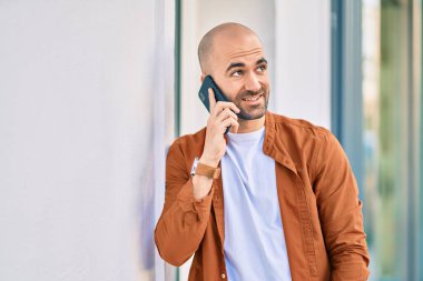 Genç, kel, gülümseyen, mutlu, akıllı telefondan konuşan bir adam..