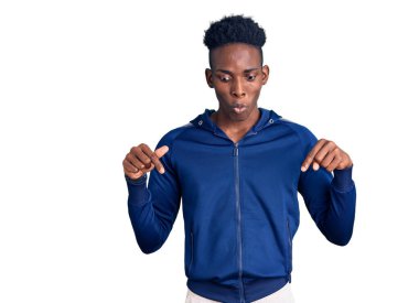 Afro-Amerikalı genç adam spor giysisi giyiyor. Parmakla işaret ediyor. Reklam yapıyor, şaşırıyor ve ağzını açıyor. 