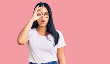 Genç, güzel Asyalı bir kız günlük kıyafetler ve gözlük takıyor. Şaşırmış yüz ifadesiyle şaşırmış, parmaklarından bakan gözler. İnançsız ifade. 