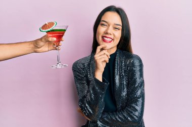 Seksi parti ceketi giyen ve İspanyol kolu olan genç bir kız kameraya gülümseyen bir kokteyl sunuyor. Kollarını kavuşturup çenesini kapatıyor. Olumlu düşünmek. 