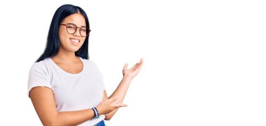 Genç, güzel Asyalı bir kız günlük kıyafetler ve gözlük takıp gülümseyerek içeri girmeye davet ediyor. 