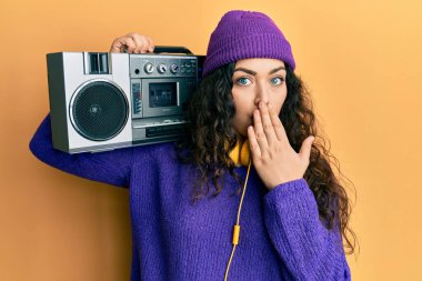 Kıvırcık saçlı, müzik kutusunu tutan, ağzı elle kaplanmış müzik dinleyen, şok olmuş ve hata yapmaktan korkan genç esmer kadın. şaşırmış ifade 