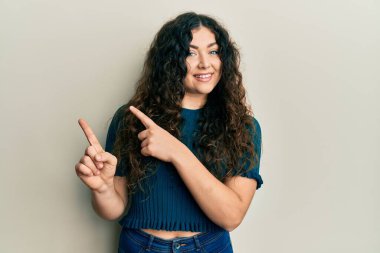 Kıvırcık saçlı genç esmer kadın. Günlük kıyafetler giyiyor. Gülümsüyor ve kameraya bakıyor.. 