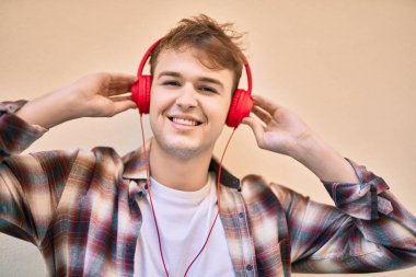 Genç beyaz adam şehirde kulaklık takarak mutlu bir şekilde gülümsüyor..