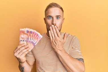 Güney Afrika 'nın 50 rand banknotunu elinde tutan genç beyaz adam ağzını eliyle kapatıyor, şok geçiriyor ve hata yapmaktan korkuyor. şaşırmış ifade 