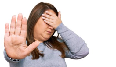 Güzel esmer ve cüsseli bir kadın, gündelik kıyafetler giyiyor, elleriyle gözleri örtüyor ve üzgün ve korku ifadeleriyle jestleri durduruyor. utangaç ve olumsuz kavram. 