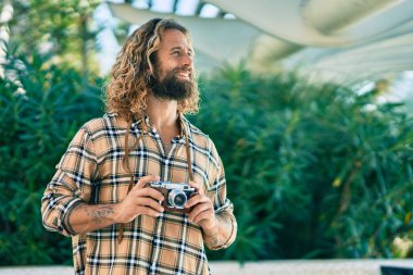 Beyaz tenli genç turist parkta klasik kamera kullanarak mutlu bir şekilde gülümsüyor..