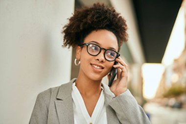Genç afro-amerikan iş kadını gülümseyerek şehirdeki akıllı telefondan konuşuyor..