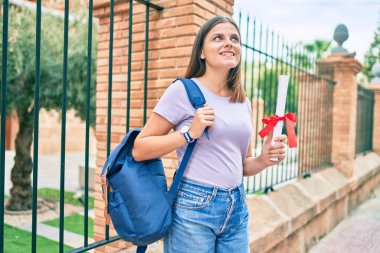 Üniversite kampüsünde diplomasını tuttuğu için mutlu gülümseyen genç bir ortadoğu öğrencisi..