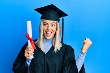 Mezuniyet şapkası ve tören cübbesi giyen güzel sarışın kadın gururla bağırıyor, zaferi kutluyor ve kollarını kaldırarak çok heyecanlanıyor. 