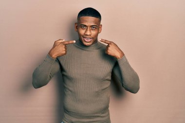 Balıkçı yaka kazak giyen, neşeli gülümseyen, parmakları, dişleri ve ağzı olan genç siyahi bir adam. diş sağlığı kavramı. 