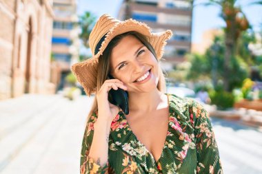 Güneşli bir günde mutlu gülümseyen güzel beyaz kadın telefonda konuşuyor.