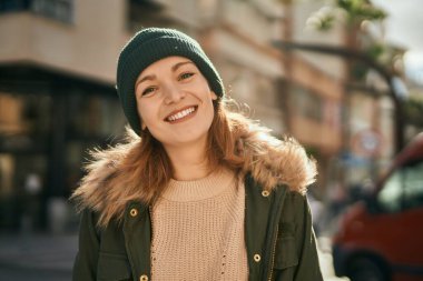 Genç beyaz kız gülümseyerek şehirde mutlu mesut duruyor..