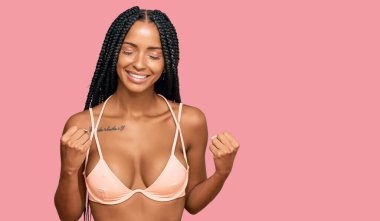 Beautiful hispanic woman wearing bikini excited for success with arms raised and eyes closed celebrating victory smiling. winner concept. 