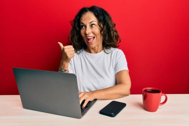 Ofiste çalışan orta yaşlı güzel bir kadın bilgisayarı kullanıyor. Parmak ucunda ağzı açık bir şekilde gülümsüyor. 