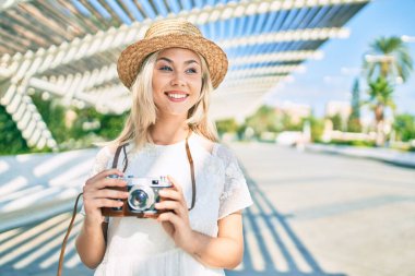Beyaz tenli genç turist kız şehrin caddesinde klasik kamera kullanarak mutlu bir şekilde gülümsüyor..