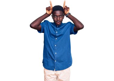 Genç, Afro-Amerikan bir adam, günlük kıyafetler giyip, boynuzları üzerinde parmaklarıyla komik jestler yapıyor. 