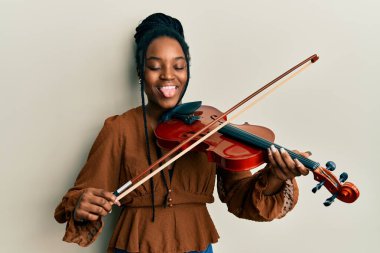 Saçları örgülü, keman çalan, komik bir ifadeyle dilini dışarı çıkaran Afrikalı Amerikalı bir kadın.. 