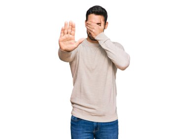 Latin kökenli genç bir adam, günlük kıyafetler giyip, elleriyle gözlerini kapatıyor ve üzgün ve korku ifadeleriyle jestleri durduruyor. utangaç ve olumsuz kavram. 