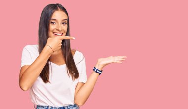 Gündelik beyaz tişört giyen genç İspanyol kadın kameraya hayret ediyor ve gülümsüyor.. 