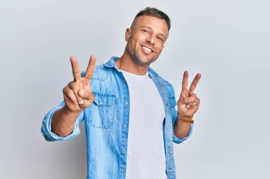 Yakışıklı, sıradan bir kot ceket giyen, gülümseyen, parmaklarını zafer işareti yaparken gösteren kaslı bir adam. İki numara.. 